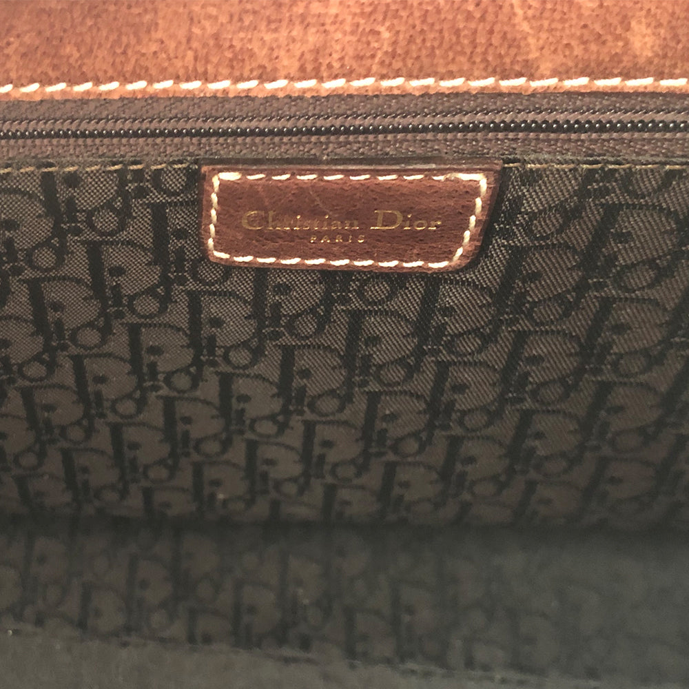 Christian Dior Canvas Saddle Tote by John Galliano. Olive canvas with brown leather handles and sides with front hanging brass logo D, accent stitching throughout. CD stamped brass-tone studs and links. Magnetic button closure. Brown Dior logo satin lining, suede and leather detail and side panels, single zip interior pocket. Brass-tone metal feet.