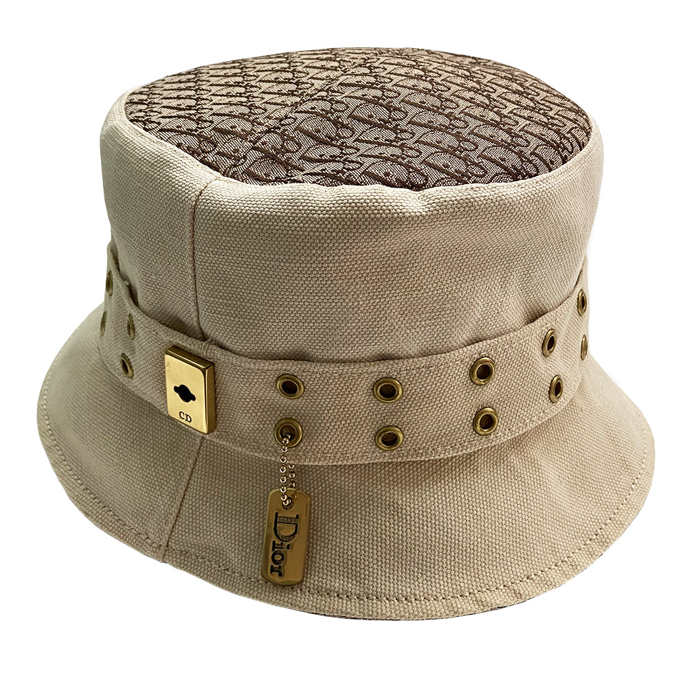 Christian Dior Street Chic Diorissimo Bucket Hat, S/S 2002 Street Chic collection by John Galliano. Light cream color canvas with tonal stitching and Diorissimo monogram logo fabric on top and under brim. Exterior band with antique brass-tone grommets and gold-tone pouch attachment and gold-tone Dior logo dog tag. Made in France