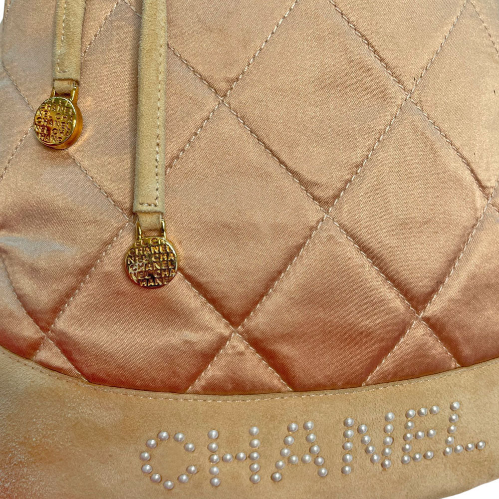 Chanel pink quilted satin and tan suede soft backpack by Karl Lagerfeld for Chanel 2001 with suede drawstring closure, silver-tone Chanel stamped tips and suede straps. Embedded faux pearls spell-out CHANEL embellishment on exterior suede satin interior with single slip pocket. Folds down flat. Made in France