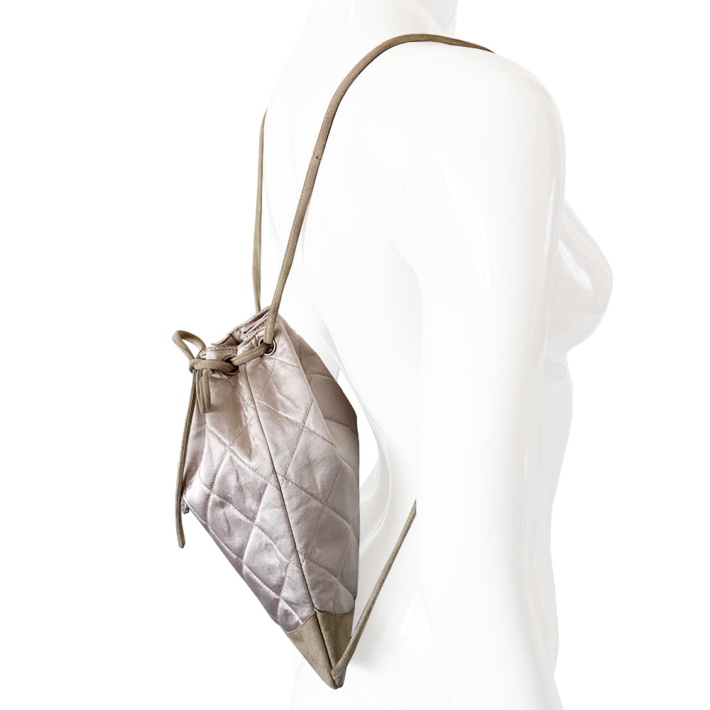 Chanel quilted satin soft backpack by Karl Lagerfeld for Chanel 2001 with suede straps and suede drawstring closure, silver-tone Chanel stamped tips. Embedded faux pearls spell-out CHANEL on exterior suede. Satin interior with single slip pocket. Date code tag attached. Periwinkle satin with tan suede. Made in France