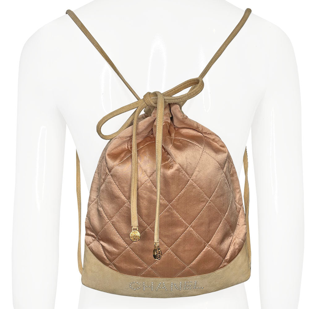 Chanel pink quilted satin and tan suede soft backpack by Karl Lagerfeld for Chanel 2001 with suede drawstring closure, silver-tone Chanel stamped tips and suede straps. Embedded faux pearls spell-out CHANEL embellishment on exterior suede satin interior with single slip pocket. Folds down flat. Made in France