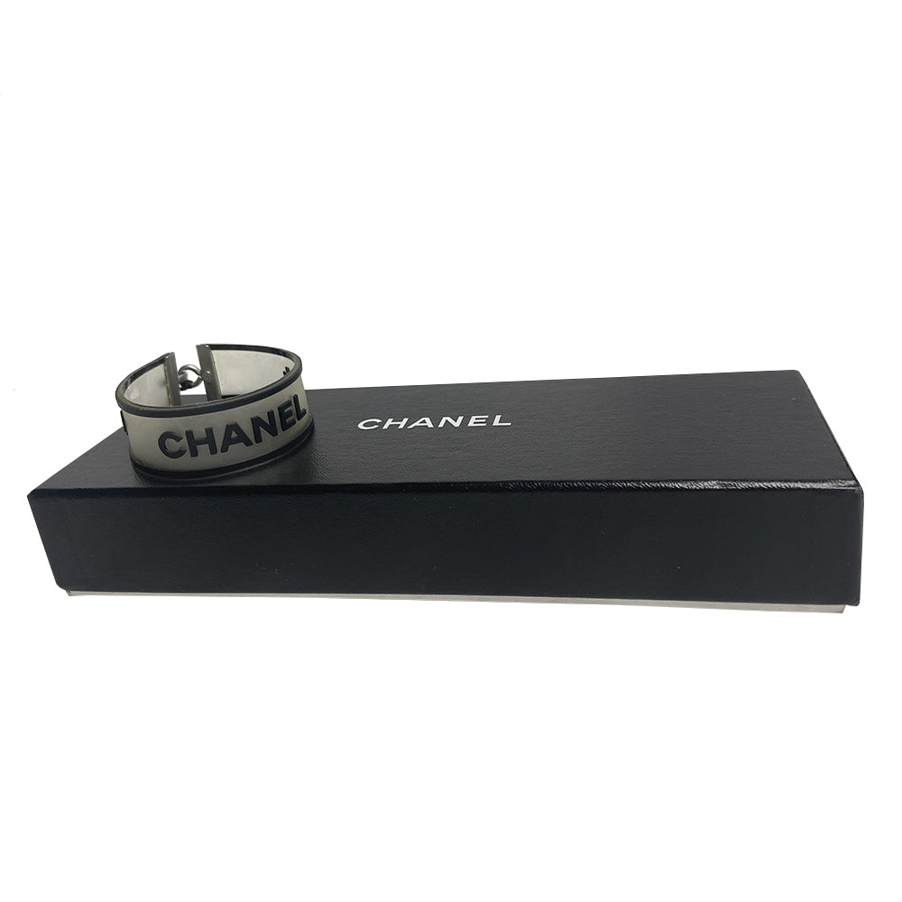Chanel rubber bracelet by Karl Lagerfeld for Chanel, Autumn 2001 with translucent with black edges tinted rubber bracelet with CHANEL printed out and 2 clovers at each end in black. Silver-tone end caps and hook closure, Chanel hallmark makers mark stamp. Made in France