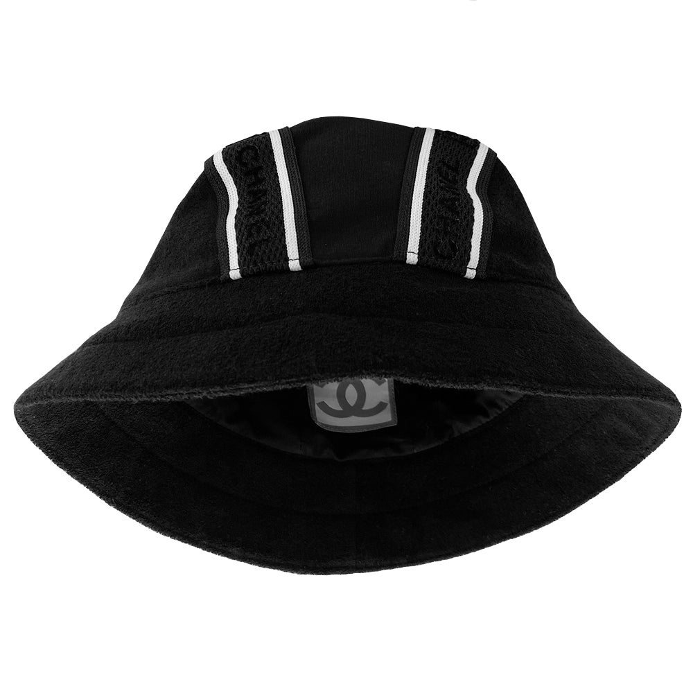 Chanel Logo Bucket Hat From 2002 sport collection Terry cloth side panels with jersey center panel rounded bucket hat embellished with 2 black and white edged mesh bands dividing the panels Chanel and boxed CC logos printed in velvet on mesh bands Color: black with white Size: M Fabric: Terry cloth, jersey, cotton interior Made in France Interior circumference (in) 22" Brim (in) 2.5"