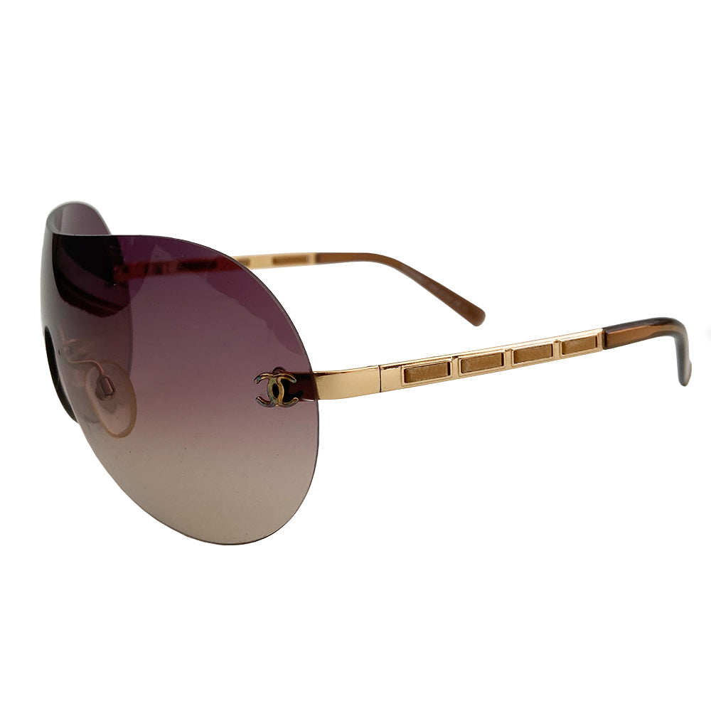 Chanel CC Leather Threaded Shield Sunglasses from mid 2000’s Oversized dark bronze gradient single shield lense and gold-tone metal arms with leather threaded through each arm. CC logo in gold on either side of frame at arm. Black quilted case included. Made in Italy.