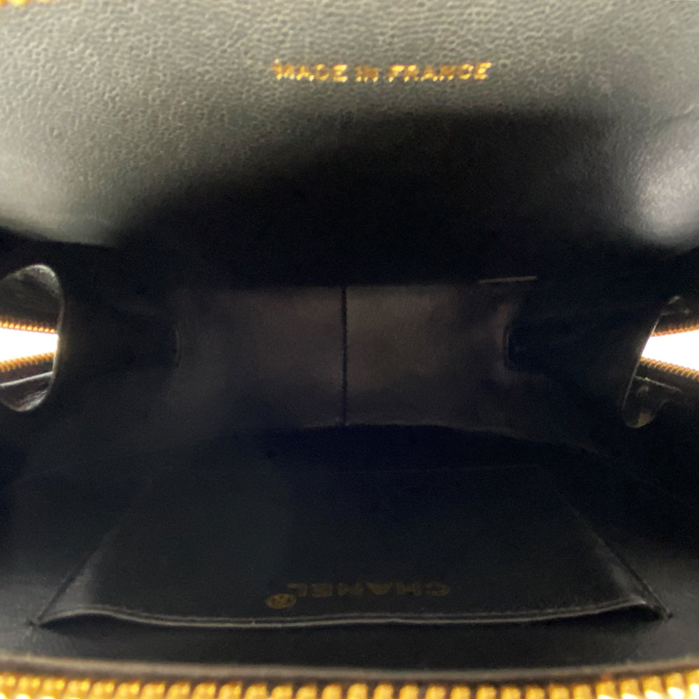 Chanel round diamond quilted black patent vanity case by Karl Lagerfeld for Chanel 1994-1996 with white interlocking appliqué CC logo at front, interwoven leather and gold chain top handle. Dual gold-tone zip around closure open to black leather interior with single slip pocket. Made in France