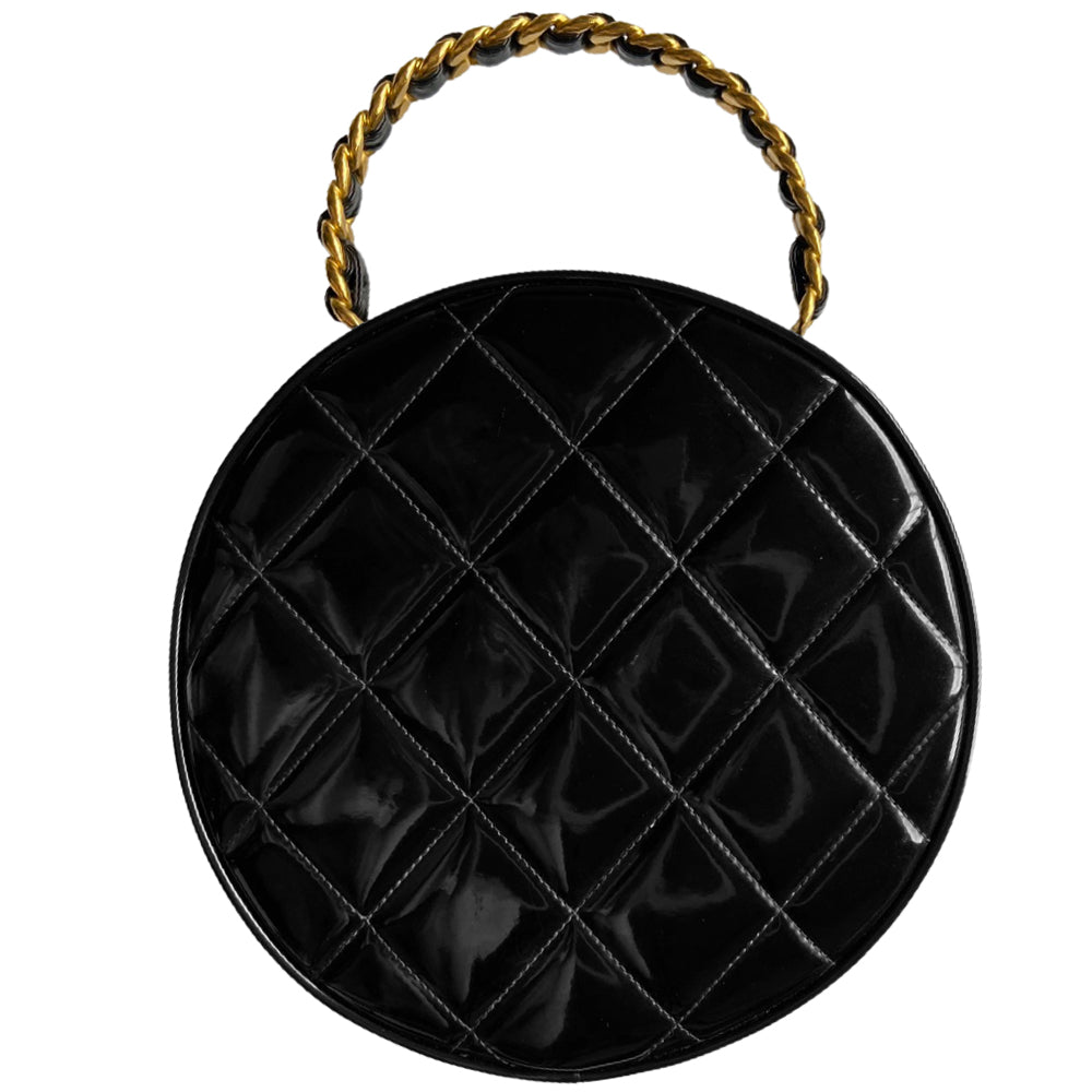 Chanel round diamond quilted black patent vanity case by Karl Lagerfeld for Chanel 1994-1996 with white interlocking appliqué CC logo at front, interwoven leather and gold chain top handle. Dual gold-tone zip around closure open to black leather interior with single slip pocket. Made in France