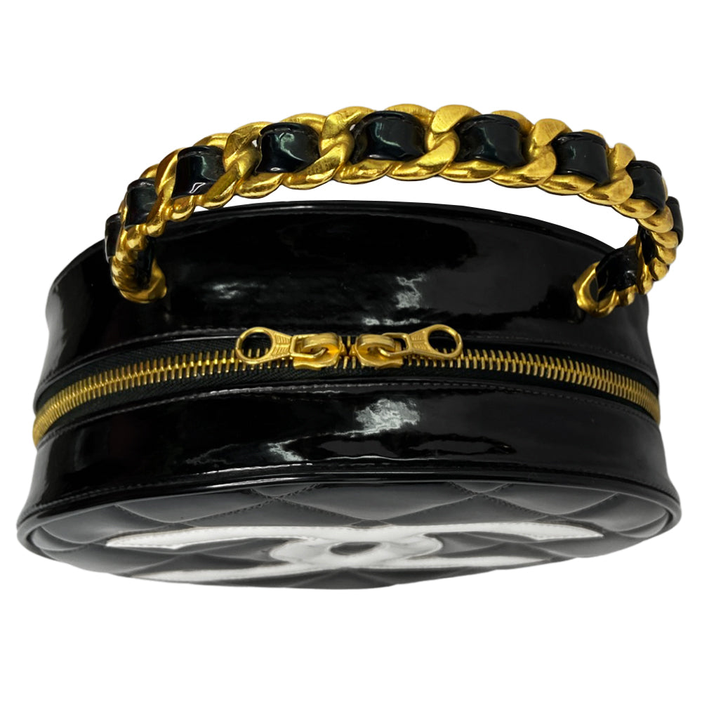 Chanel round diamond quilted black patent vanity case by Karl Lagerfeld for Chanel 1994-1996 with white interlocking appliqué CC logo at front, interwoven leather and gold chain top handle. Dual gold-tone zip around closure open to black leather interior with single slip pocket. Made in France