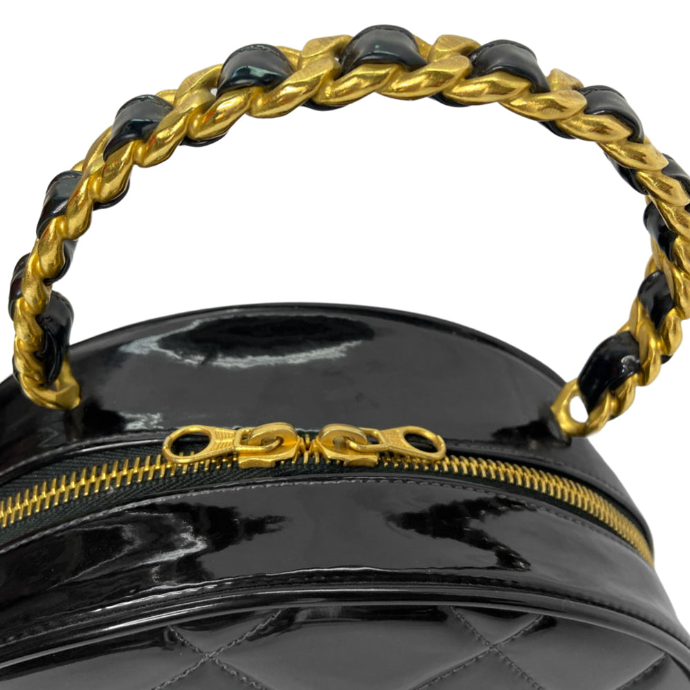 Chanel round diamond quilted black patent vanity case by Karl Lagerfeld for Chanel 1994-1996 with white interlocking appliqué CC logo at front, interwoven leather and gold chain top handle. Dual gold-tone zip around closure open to black leather interior with single slip pocket. Made in France