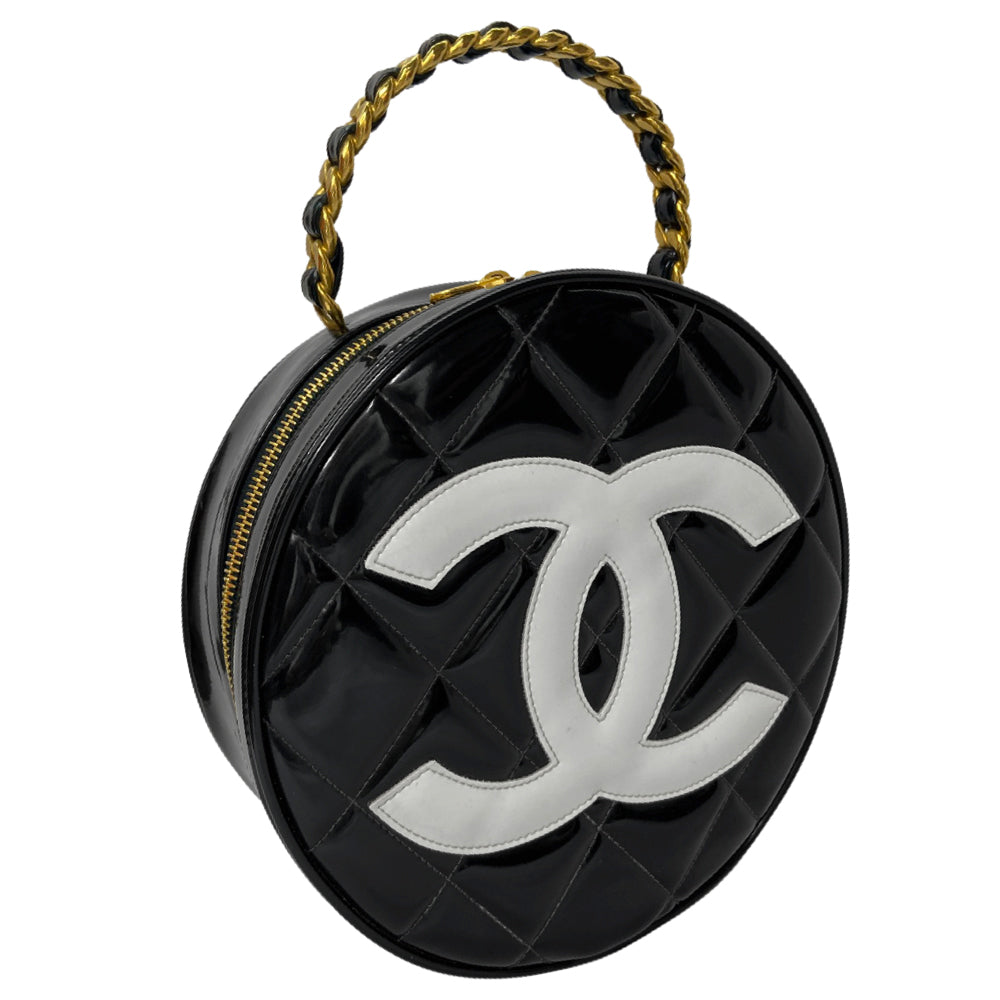 Chanel round diamond quilted black patent vanity case by Karl Lagerfeld for Chanel 1994-1996 with white interlocking appliqué CC logo at front, interwoven leather and gold chain top handle. Dual gold-tone zip around closure open to black leather interior with single slip pocket. Made in France