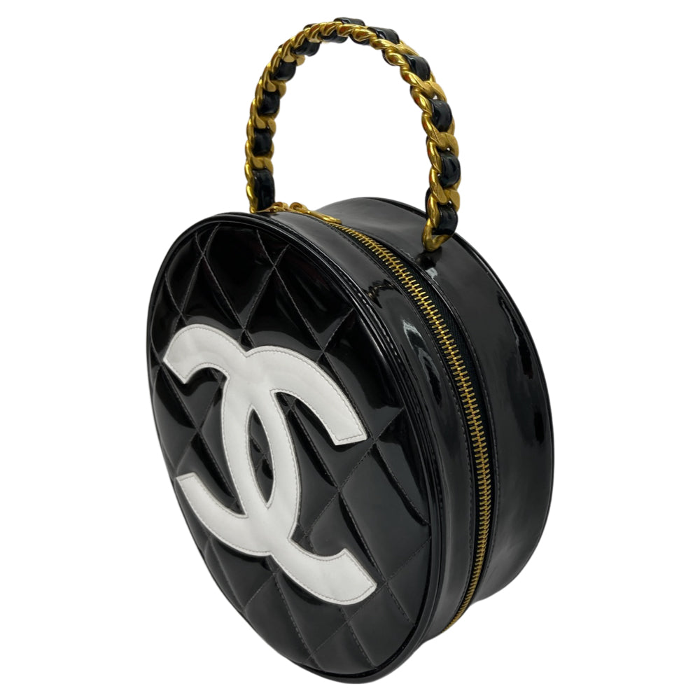 Chanel round diamond quilted black patent vanity case by Karl Lagerfeld for Chanel 1994-1996 with white interlocking appliqué CC logo at front, interwoven leather and gold chain top handle. Dual gold-tone zip around closure open to black leather interior with single slip pocket. Made in France