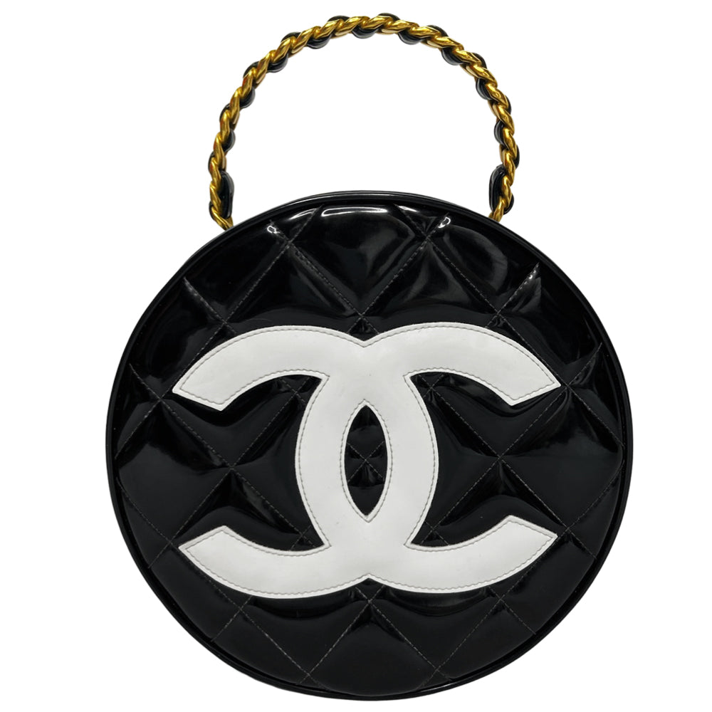 Chanel round diamond quilted black patent vanity case by Karl Lagerfeld for Chanel 1994-1996 with white interlocking appliqué CC logo at front, interwoven leather and gold chain top handle. Dual gold-tone zip around closure open to black leather interior with single slip pocket. Made in France