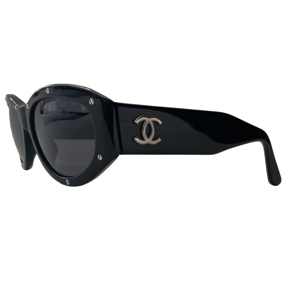 Chanel black acetate frame studded sunglasses from 1990’s Karl Lagerfeld for Chanel featuring 10 silver-tone screw studs inset into the frame. Thick side arms with silver-tone interlocking CC logo at temples and charcoal lenses. Style: 06918 94305. Made in Italy