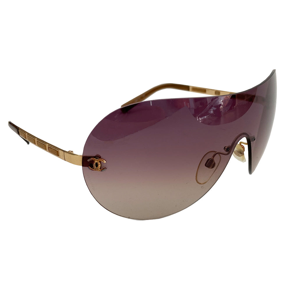 Chanel CC Leather Threaded Shield Sunglasses from mid 2000’s Oversized dark bronze gradient single shield lense and gold-tone metal arms with leather threaded through each arm. CC logo in gold on either side of frame at arm. Black quilted case included. Made in Italy.