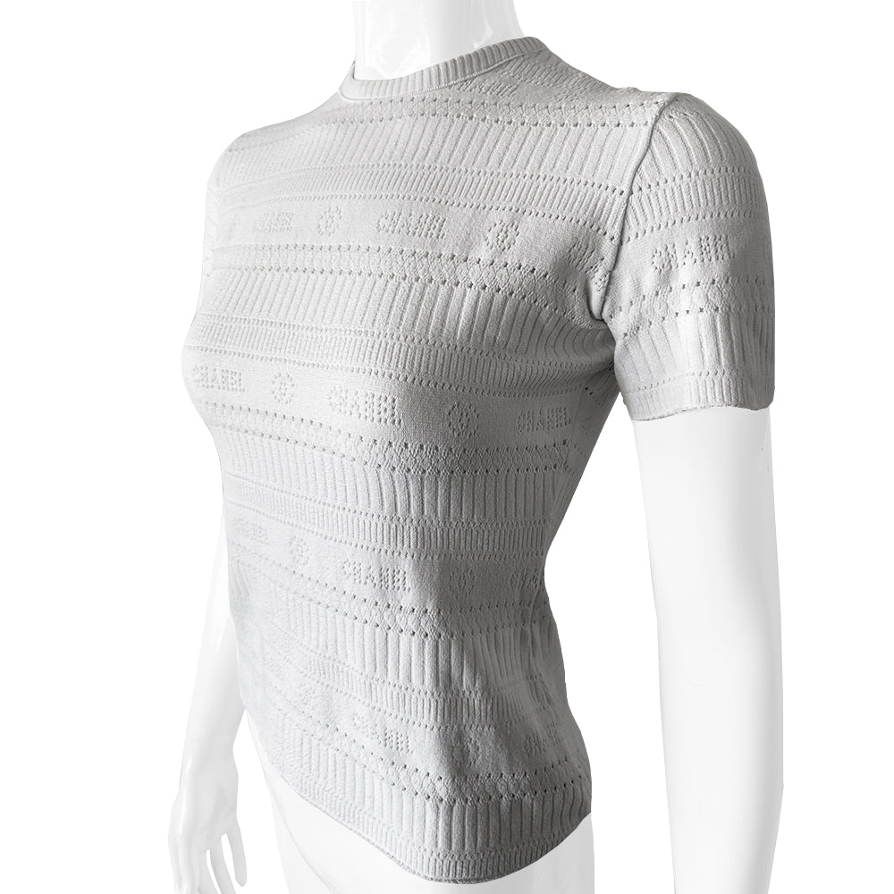 Chanel white ribbed perforated knit top by Karl Lagerfeld for Chanel, Spring 1997. Crew neck, all white short sleeved tee with perforations at ribbing edges and small woven diamond patterns to form horizontal stripes and 4 alternating rows of tiny perforations that form the word CHANEL. Made in France.