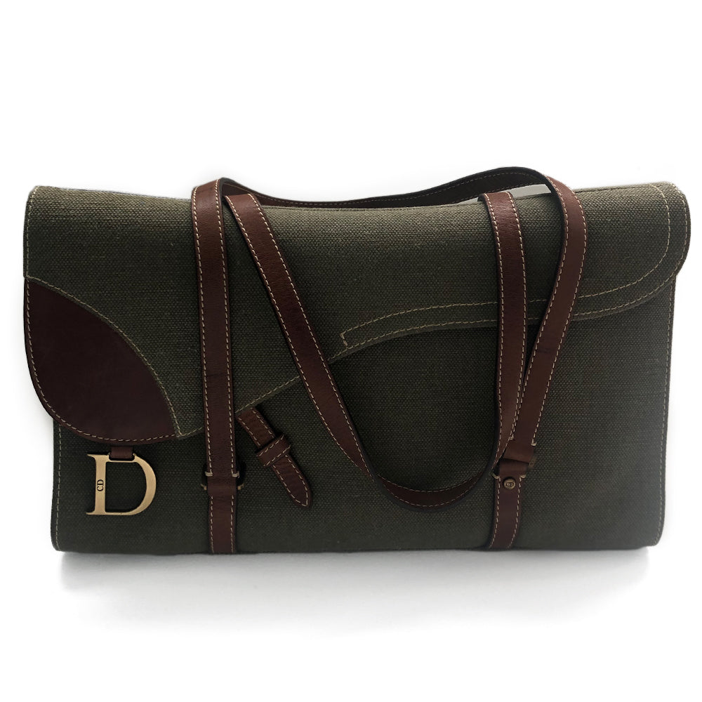Christian Dior Canvas Saddle Tote by John Galliano. Olive canvas with brown leather handles and sides with front hanging brass logo D, accent stitching throughout. CD stamped brass-tone studs and links. Magnetic button closure. Brown Dior logo satin lining, suede and leather detail and side panels, single zip interior pocket. Brass-tone metal feet.