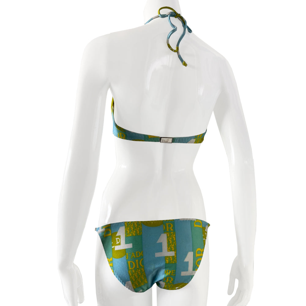 Christian Dior J’Adore Dior iconic logos bikini, spring 2005 RTW runway, John Galliano for Dior. Underwire bra with faux tie front, silver-tone engraved logo clasp back closure, ties behind the neck and silver-tone letter blocks spell out DIOR on one side. Bottoms with silver tone letter blocks spell out DIOR. Made in France