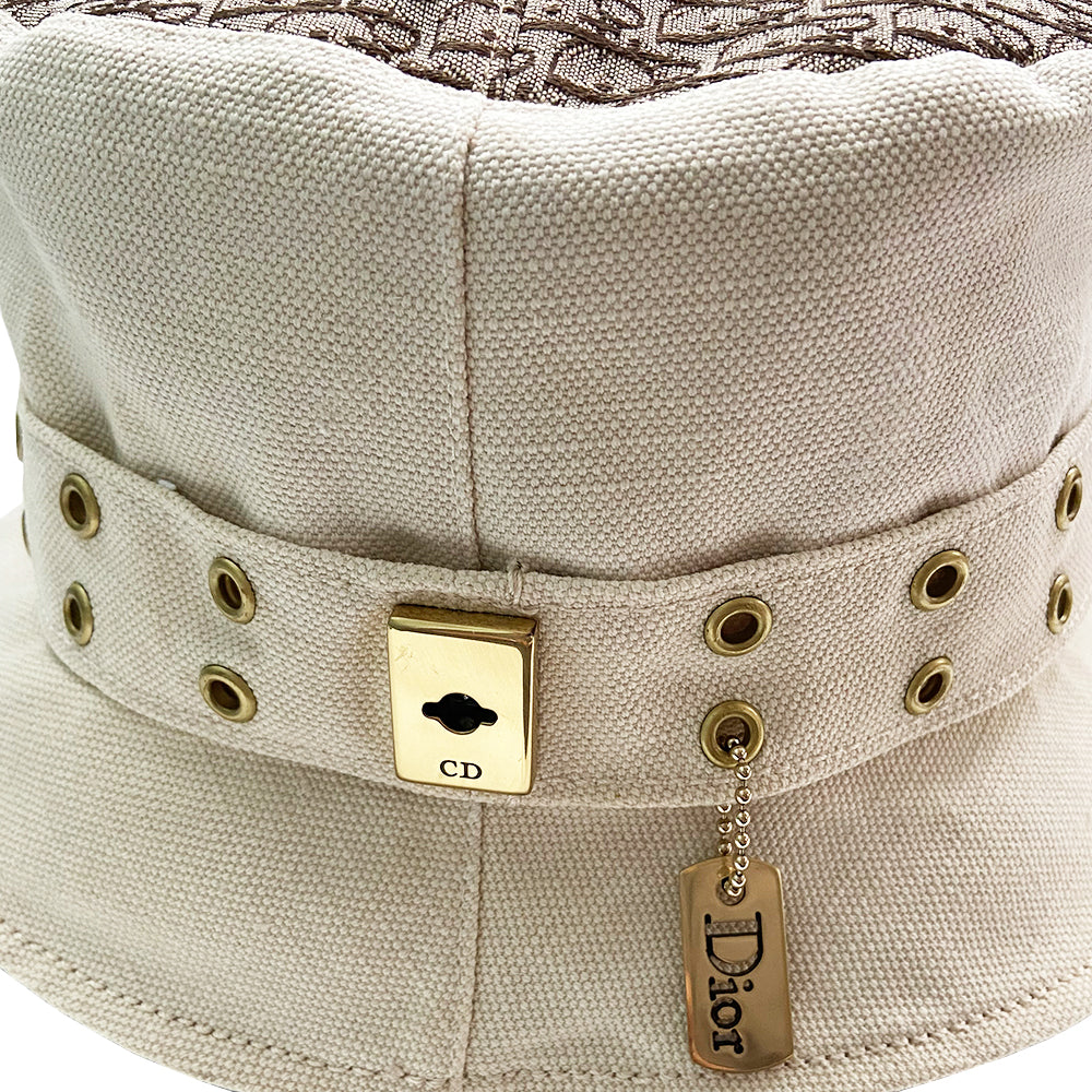 Christian Dior Street Chic Diorissimo Bucket Hat, S/S 2002 Street Chic collection by John Galliano. Light cream color canvas with tonal stitching and Diorissimo monogram logo fabric on top and under brim. Exterior band with antique brass-tone grommets and gold-tone pouch attachment and gold-tone Dior logo dog tag. Made in France