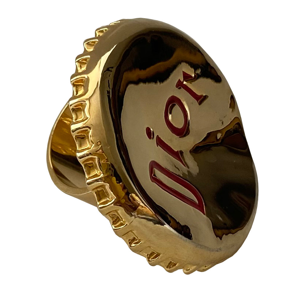 Christian Dior Logo Bottle Cap ring circa 2004. Gold-tone "bent” bottle cap ring with red embossed logo and thick band. Adjustable band for various sizing. Dior box and booklet included.