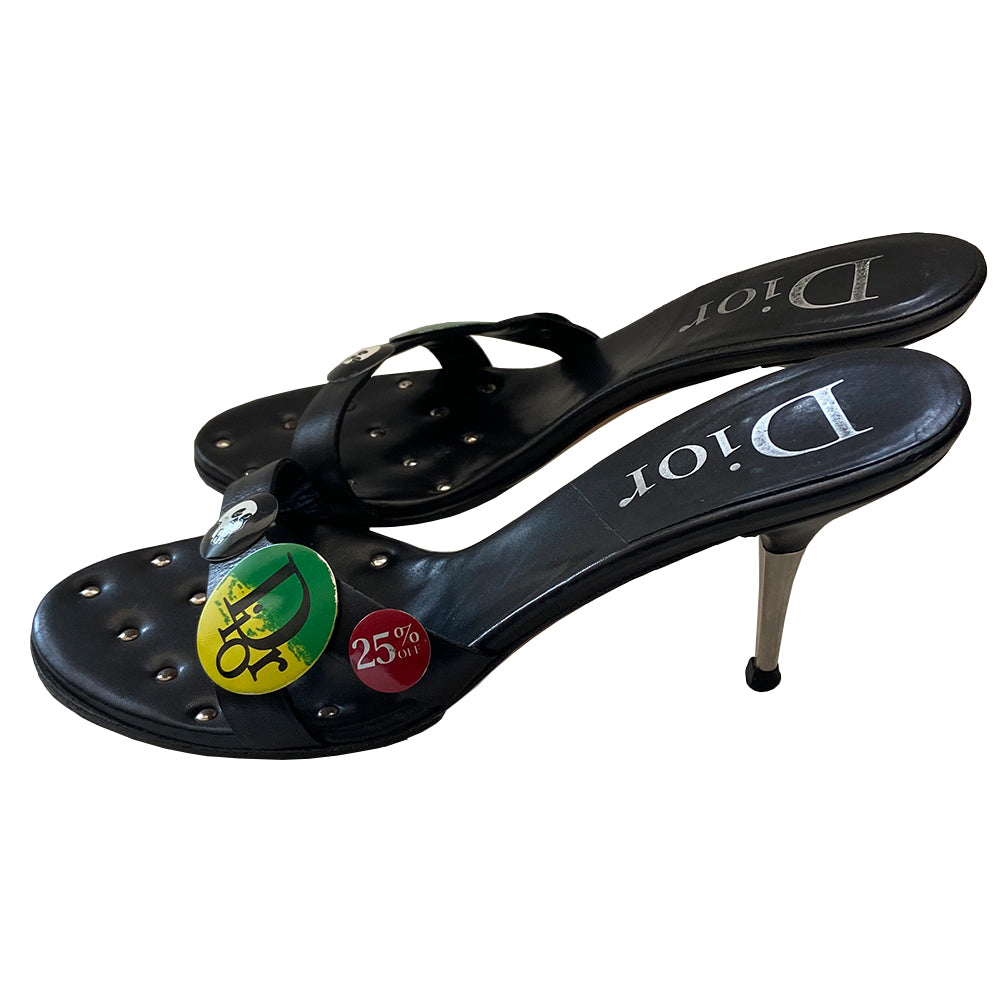 Christian Dior black leather slip-on open toe sandals with silver-tone metal high heels, John Galliano for Dior Spring 2003 with skull, Dior logo and 25% off badges attached to upper leather straps. Leather with silver-tone stud tufting inside front insole. Black with green, yellow, red, white buttons. Made in Italy