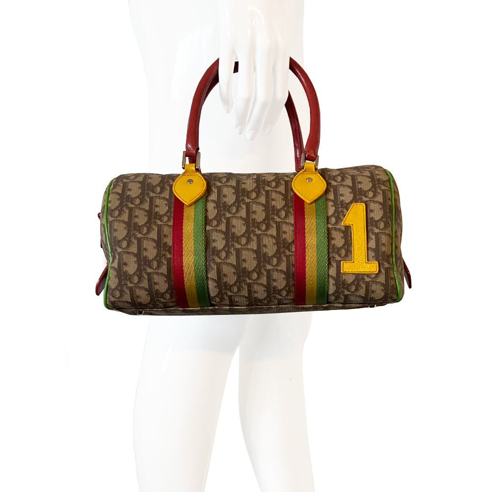 Christian Dior Rasta Boston Bag by John Galliano, 2003 beige and brown Diorissimo coated canvas, silver-tone hardware, vermillion leather rolled handles, yellow accent at base of handles. Yellow #1 front. Red, yellow and green canvas stripe on beige and brown Diorissimo print with bright green piping. Bottom domed silver-tone feet, single interior zip pocket and zip closure at top Vermillion textile interior, single zip pocket.