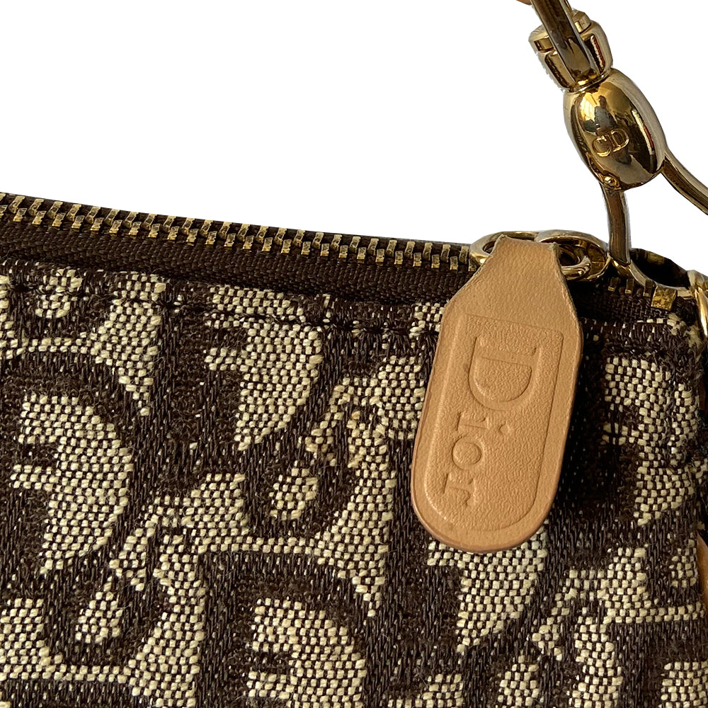 Christian Dior brown monogram canvas mini saddle pochette by John Galliano for Dior, 2001 with tan leather piping and strap with gold-tone hardware. Leather strap unclips at one end and can be looped to carry wristlet style. Top zip closure with Dior embossed leather zipper pull, brown textile interior. Made in Spain