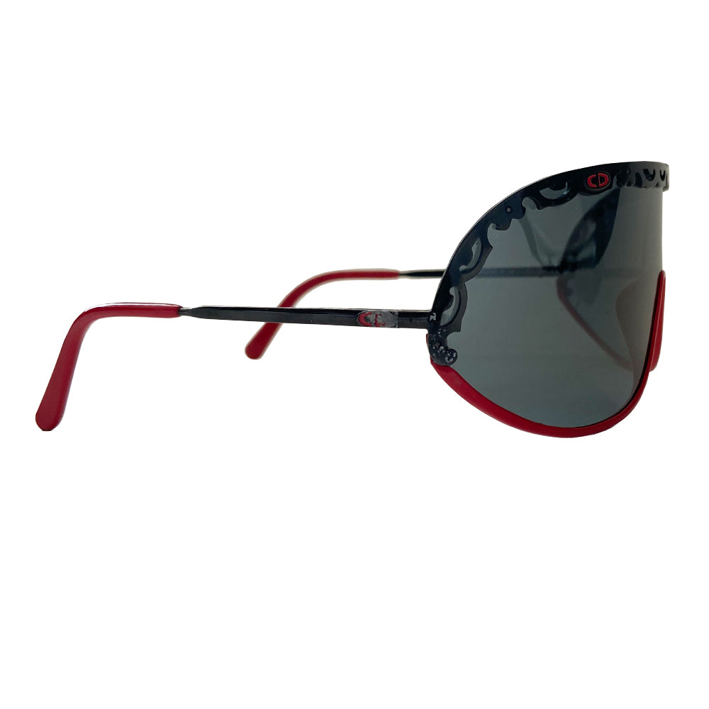 Christian Dior shield sunglasses circa 1980’s. Oversized shield lens with delicate black metal lace design along the top, with red accent metal rim at lower frame Vintage style Dior logo engraved on arms. Lens Color: Dark grey Style: 2501 93/110 Dior case included. Made in Austria