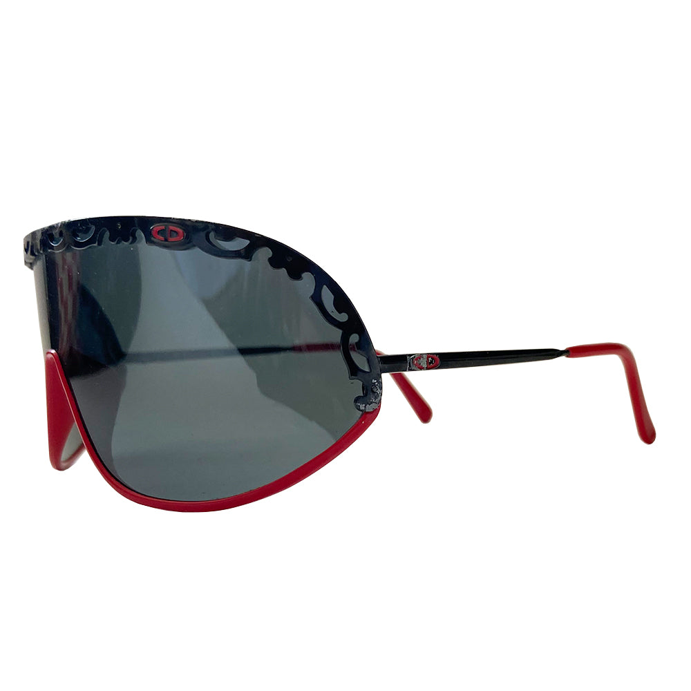 Christian Dior shield sunglasses circa 1980’s. Oversized shield lens with delicate black metal lace design along the top, with red accent metal rim at lower frame Vintage style Dior logo engraved on arms. Lens Color: Dark grey Style: 2501 93/110 Dior case included. Made in Austria