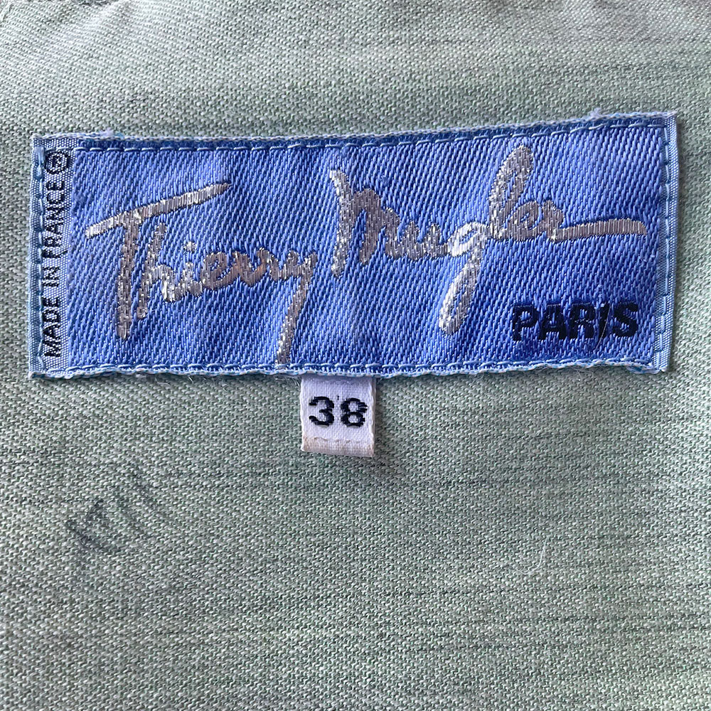 Thierry Mugler 1980's seafoam green wool jacket with angled front flap featuring the iconic Mugler wave, green acetate belt and triangle buttons. Three front snap closures, two at waist and one at chest, back pleats and blouson body. Made in France