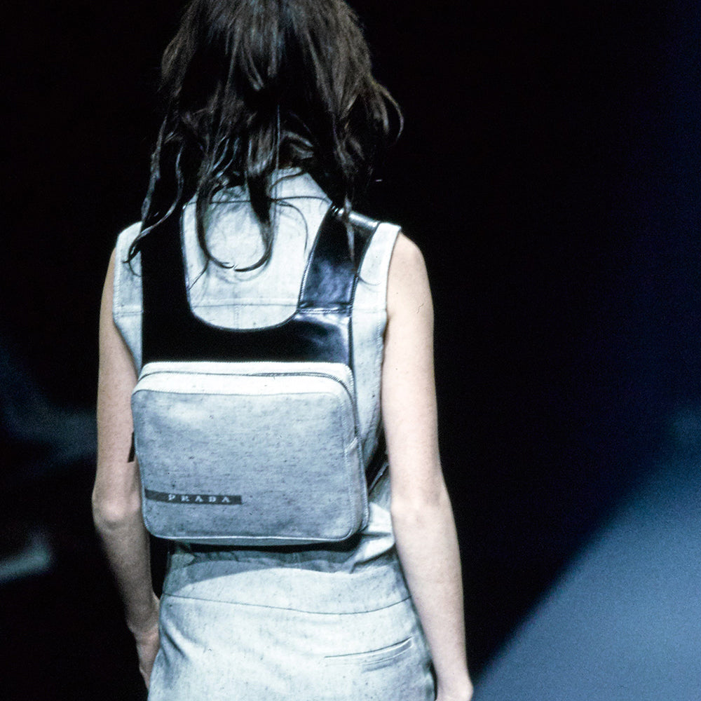 Prada spring 1999 RTW runway backpack in black and white tweed with black leather backing, adjustable leather harness straps, silver-tone hardware. Top zipper opens to jacquard logo textile lining with interior zip pocket. Made in Italy