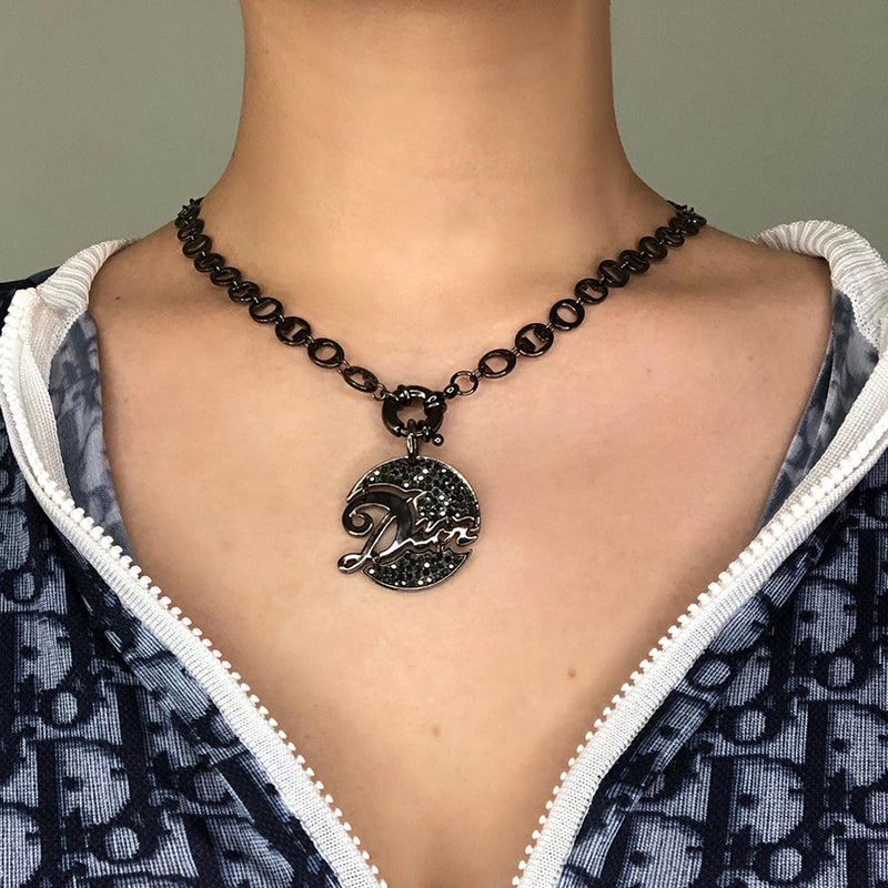 Christian Dior graphite-tone charm necklace. 9.25” chain links spell DIOR. Graphite tone crystals surround Dior signature pendant with front toggle clasp. 