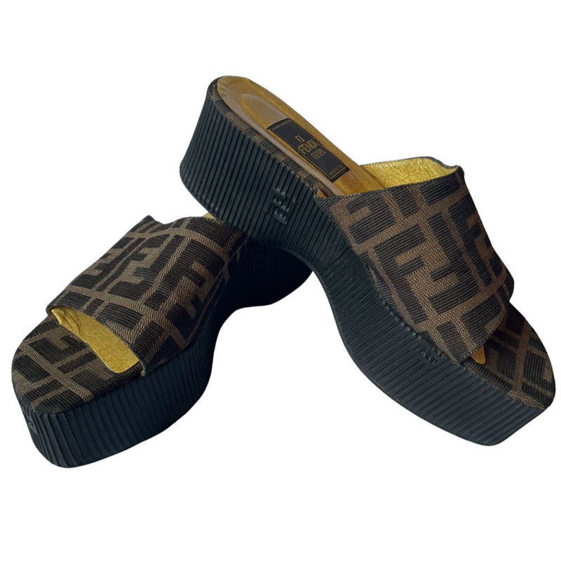 Fendi brown Zucca print fabric upper slip-on open toe slides with 2.5” black ribbed edge platform with small heel. Leather insoles with zucca fabric at inner sole toe, Fendi logo on inner sole, FF logos imprinted at outer platform. Made in Italy.