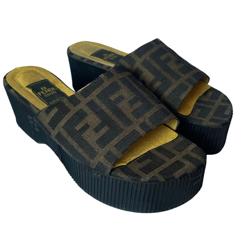 Fendi brown Zucca print fabric upper slip-on open toe slides with 2.5” black ribbed edge platform with small heel. Leather insoles with zucca fabric at inner sole toe, Fendi logo on inner sole, FF logos imprinted at outer platform. Made in Italy.