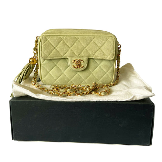 Chanel suede camera bag by Karl Lagerfeld for Chanel, 1991-94. Pistachio color quilted suede, top zipper, etched gold ball and tassels zipper pull, suede and gold chain shoulder strap. Outer flap pocket with engraved gold CC turn-lock, tonal leather lining, patch slip and zippered pocket with gold zipper pull. Made in France 