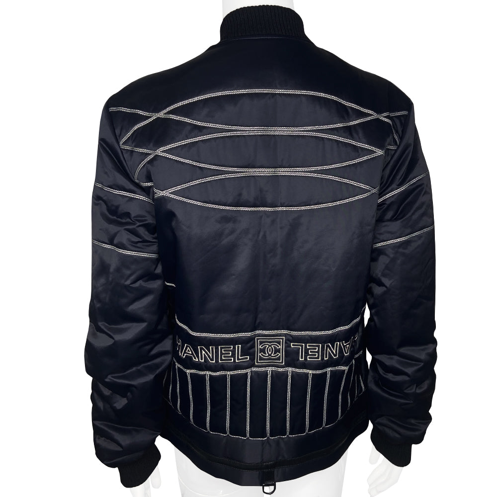 Chanel CC logo long sleeve black satin zip jacket by Karl Lagerfeld for Chanel, AW 2006 with side pockets, rib knit collar and cuffs, lamb leather accent, front zip, 2 buckle closure. CC engraved padlock zipper pull. White appliqué cording accents on front, back and sleeve with embroidered CC box logo, CHANEL in back, metal D-ring. Made in Italy 