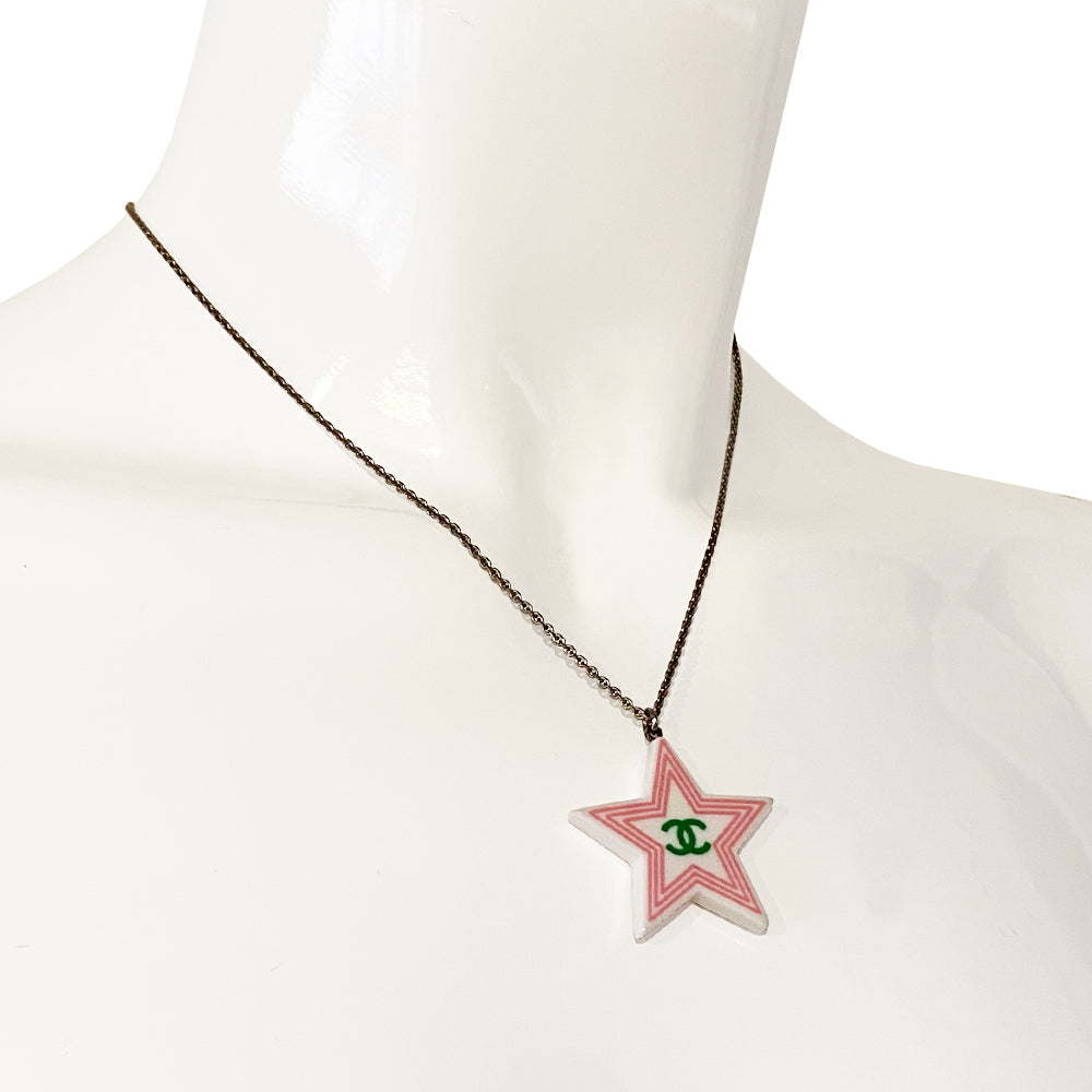 Chanel 2 sided white resin star pendant necklace by Karl Lagerfeld for Chanel Cruise collection, 2004 with pink border and yellow CC logo on one side, green logo on the other. Silver-tone long chain with lobster closure, interlocking metal CC logo charm at one end and metal stamped tag attached. Made in France.
