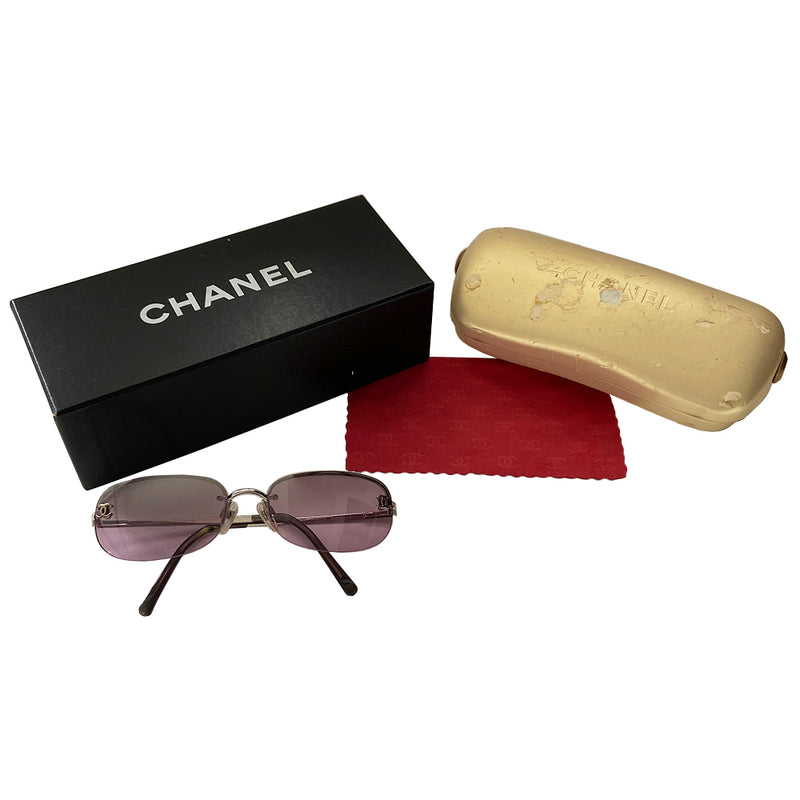 Chanel purple lens CC logo sunglasses with rounded rectangle shape, metal frame on upper lens and frameless on the bottom. Silver-tone metal frame with purple lenses, CC logo at each lens, Chanel engraved nose pad Includes case, box and dust cloth Style: 4099 C124/7A. Made in Italy 