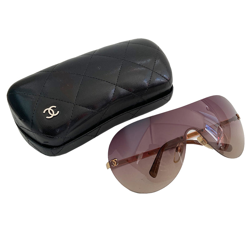 Chanel CC Leather Threaded Shield Sunglasses from mid 2000’s Oversized dark bronze gradient single shield lense and gold-tone metal arms with leather threaded through each arm. CC logo in gold on either side of frame at arm.  Black quilted case included. Made in Italy. 