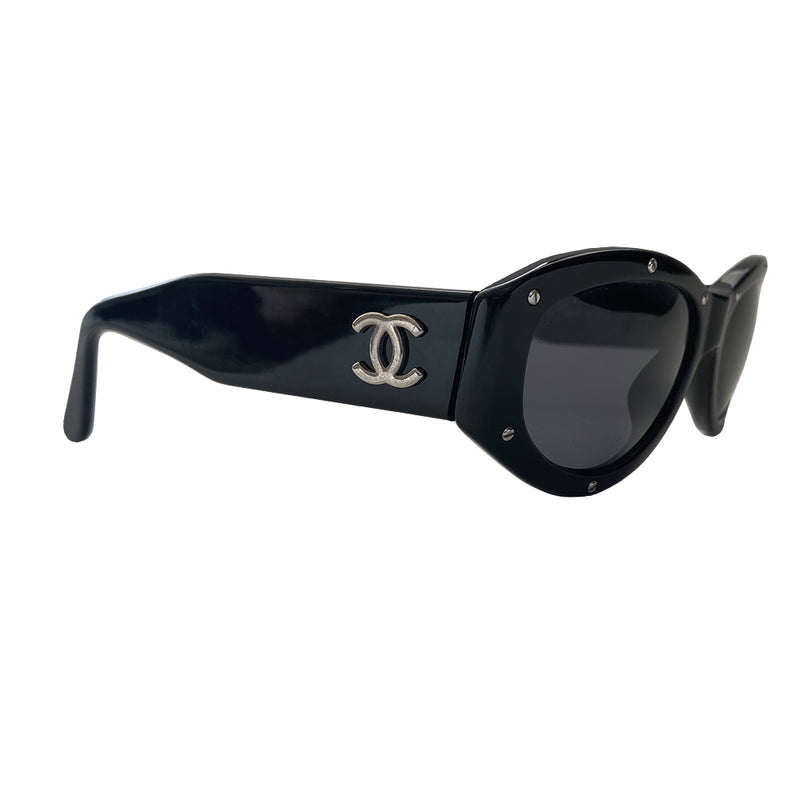 Chanel black acetate frame studded sunglasses from 1990’s Karl Lagerfeld for Chanel featuring 10 silver-tone screw studs inset into the frame. Thick side arms with silver-tone interlocking CC logo at temples and charcoal lenses. Style: 06918 94305. Made in Italy