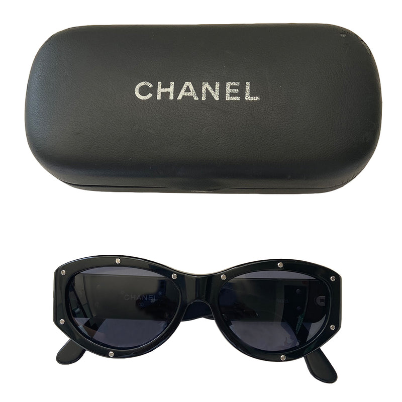 Chanel black acetate frame studded sunglasses from 1990’s Karl Lagerfeld for Chanel featuring 10 silver-tone screw studs inset into the frame. Thick side arms with silver-tone interlocking CC logo at temples and charcoal lenses. Style: 06918 94305. Made in Italy
