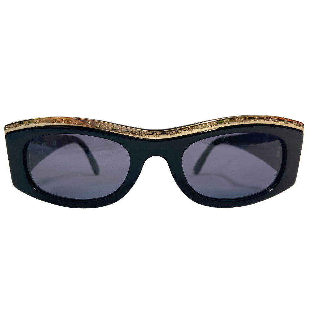 Chanel Paris CC logo black acetate frame sunglasses from the 1990’s by Karl Lagerfeld for Chanel embellished with gold-tone Chanel Paris engraved strip across the top from edge to edge and thick side arms and blue lenses. Style: 07798 94305. Made in Italy 