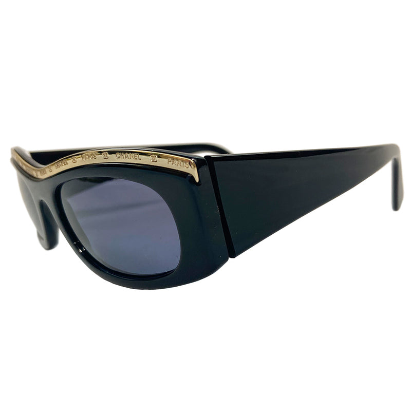 Chanel Paris CC logo black acetate frame sunglasses from the 1990’s by Karl Lagerfeld for Chanel embellished with gold-tone Chanel Paris engraved strip across the top from edge to edge and thick side arms and blue lenses. Style: 07798 94305. Made in Italy 