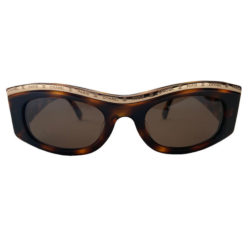 Chanel Paris CC logo tortoise sunglasses from the 1990’s, Karl Lagerfeld for Chanel. Tortoise acetate frames embellished with gold-tone Chanel Paris engraved strip across the top from edge to edge and thick side arms and dark brown lenses. Style: 07798 91235. Made in Italy