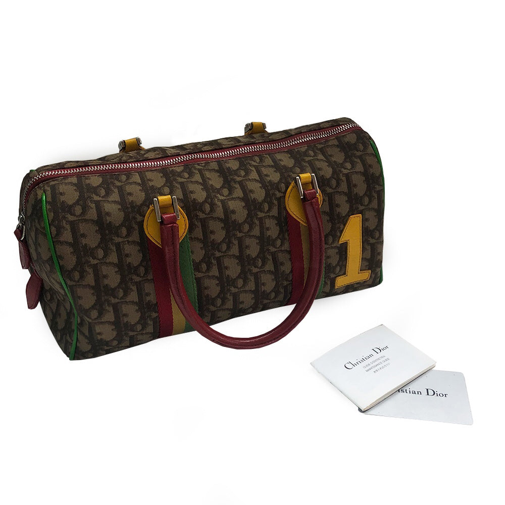 Christian Dior Rasta Boston Bag by John Galliano, 2003 beige and brown Diorissimo coated canvas, silver-tone hardware, vermillion leather rolled handles, yellow accent at base of handles. Yellow #1 front. Red, yellow and green canvas stripe on beige and brown Diorissimo print with bright green piping. Bottom domed silver-tone feet, single interior zip pocket and zip closure at top Vermillion textile interior, single zip pocket.
