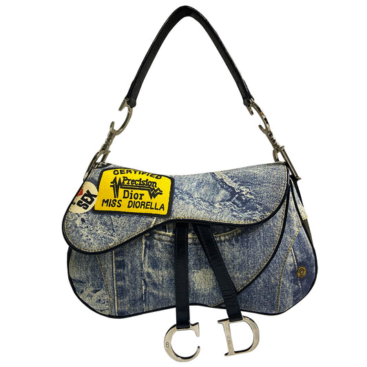 Christian Dior I Heart Sex denim saddle bag by John Galliano for Dior 2001. Trompe l’oeil blue and black denim with patch printed designs, black leather shoulder strap with silver-tone CD logo attachments, leather piping and hanging straps, silver-tone CD hanging logos. front flap, rear single slip pocket, interior zip pocket. Made in Italy 