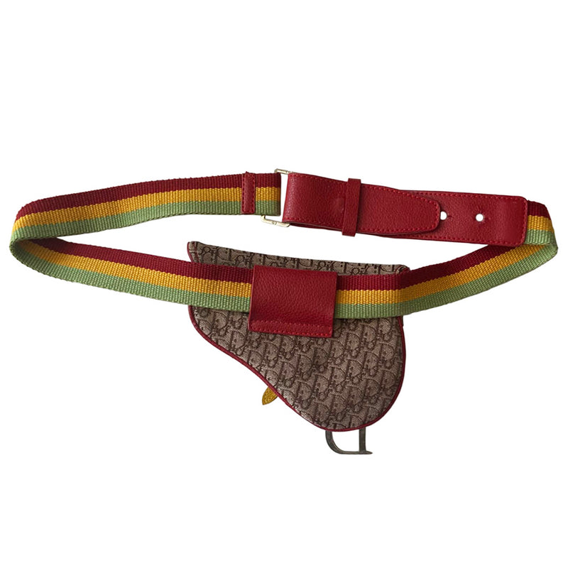 Christian Dior Rasta mini saddle belt waist bag by John Galliano for Dior 2004.  Diorissimo canvas with red leather outer piping, yellow & green accent piping, silver-tone hardware. Adjustable canvas webbing & leather belt with 5 hole pin closure. Top flap magnetic snap closure with green & yellow leather straps, CD engraved hanging D, brown satin textile interior. 