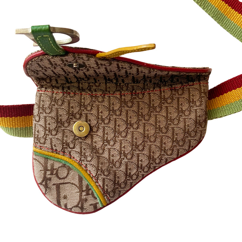 Christian Dior Rasta mini saddle belt waist bag by John Galliano for Dior 2004.  Diorissimo canvas with red leather outer piping, yellow & green accent piping, silver-tone hardware. Adjustable canvas webbing & leather belt with 5 hole pin closure. Top flap magnetic snap closure with green & yellow leather straps, CD engraved hanging D, brown satin textile interior. 