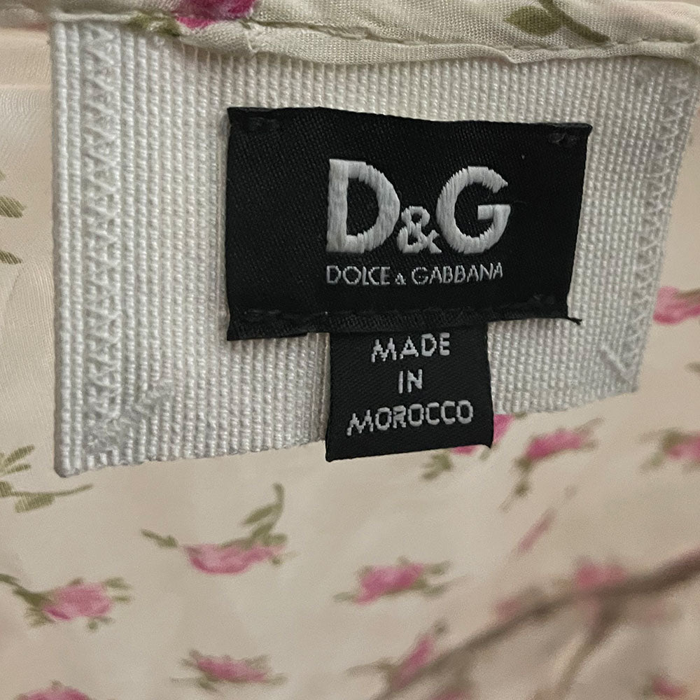 D&G silk pink and white puffed sleeve dress with D&G logo stamped button front in all over pink rosebud print. Ruffled yoke in front, back and hemline, elastic and ties at sleeves and waist. Made in Morocco 