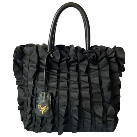 Prada 2000s black ruffled body tessuto nylon tote with leather handles, accent and hanging clochette key holder featuring gold-tone logo. Gold-tone hardware, interior logo, zippers and logo engraved feet. Magnetic snap closure, interior trademark leather label, 2 interior zip pockets, Prada logo lining. Made in Italy 