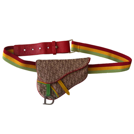 Christian Dior Rasta mini saddle belt waist bag by John Galliano for Dior 2004.  Diorissimo canvas with red leather outer piping, yellow & green accent piping, silver-tone hardware. Adjustable canvas webbing & leather belt with 5 hole pin closure. Top flap magnetic snap closure with green & yellow leather straps, CD engraved hanging D, brown satin textile interior. 