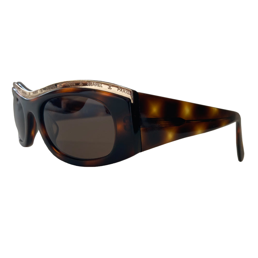 Chanel Paris CC logo tortoise sunglasses from the 1990’s, Karl Lagerfeld for Chanel. Tortoise acetate frames embellished with gold-tone Chanel Paris engraved strip across the top from edge to edge and thick side arms and dark brown lenses. Style: 07798 91235. Made in Italy